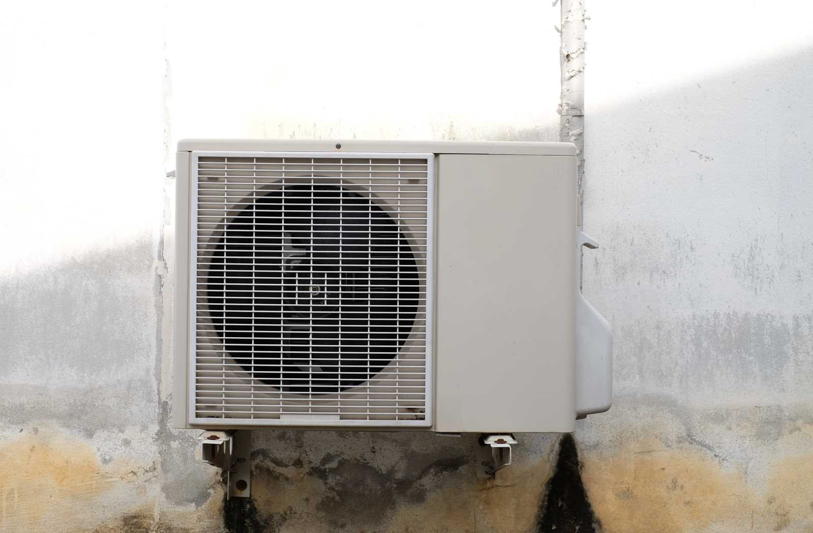 Old, rusty, noisy air conditioner mounted to a dirty wall