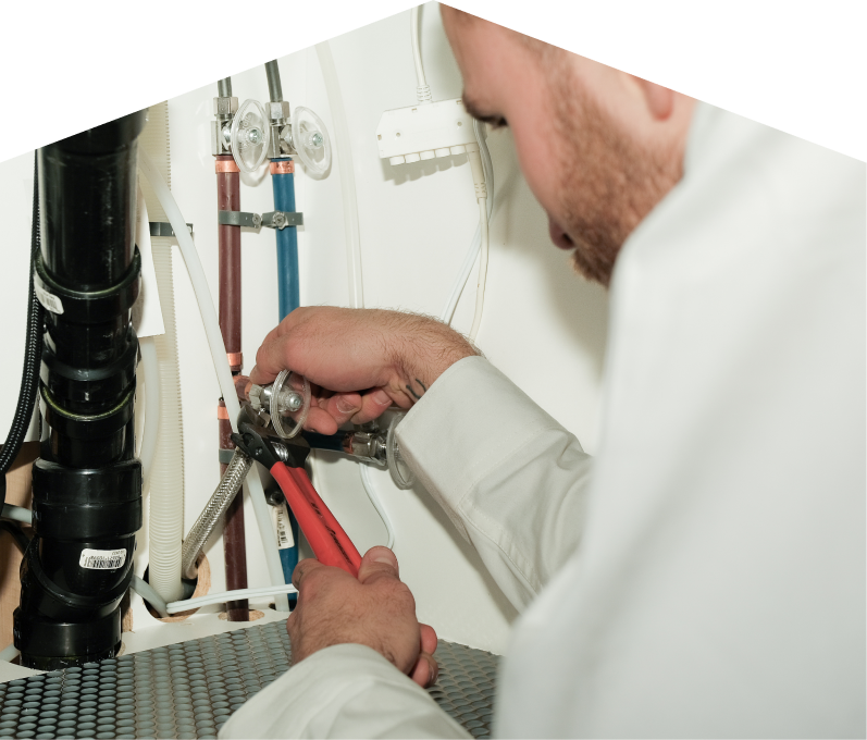 Limcan plumbing expert tightening connections under a sink during a faucet installation, surrounded by hot and cold water supply lines and PVC drainage. Limcan plumbing expert tightening connections under a sink during a faucet installation, surrounded by hot and cold water supply lines and PVC drainage.
