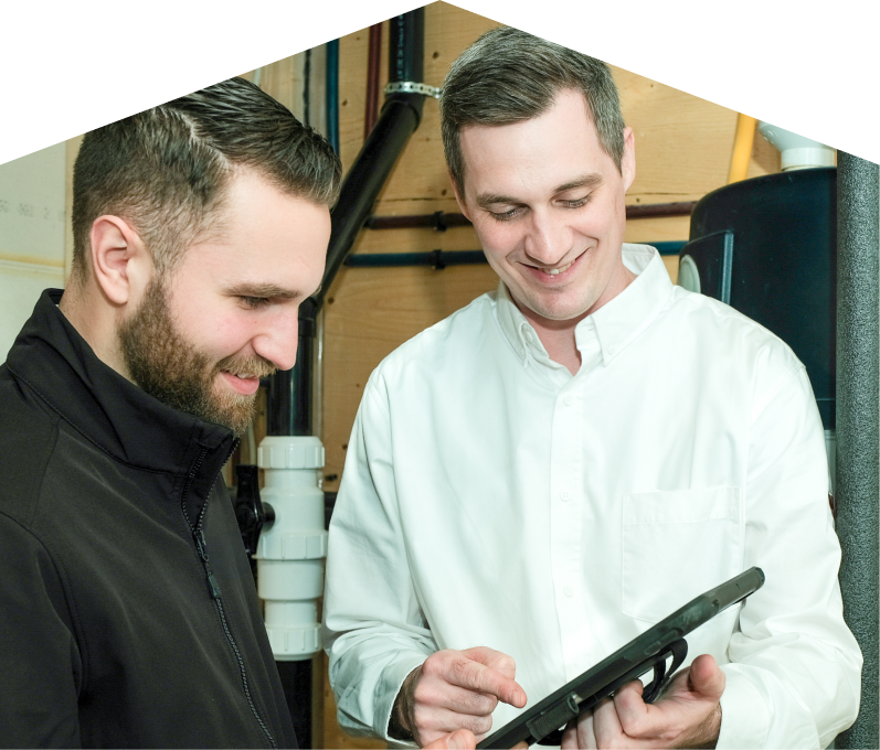 Limcan specialist reviewing maintenance plan options with a smiling homeowner using a tablet, inside a utility room with visible piping. Limcan specialist reviewing maintenance plan options with a smiling homeowner using a tablet, inside a utility room with visible piping.