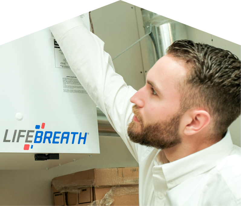 Limcan indoor air quality specialist inspects a Lifebreath ventilation unit related to UV air purifiers, with ductwork and boxes in the background. Limcan indoor air quality specialist inspects a Lifebreath ventilation unit related to UV air purifiers, with ductwork and boxes in the background.