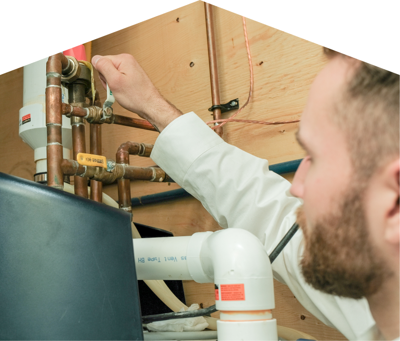 Limcan water heater specialist tightens a valve on copper piping during a water heater installation, with exposed wood paneling and wiring in the background. Limcan water heater specialist tightens a valve on copper piping during a water heater installation, with exposed wood paneling and wiring in the background.